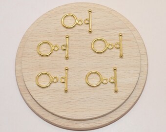 May include: Six gold-toned metal toggle clasps on a wooden surface. Each clasp has a round ring and a bar with a rounded end.