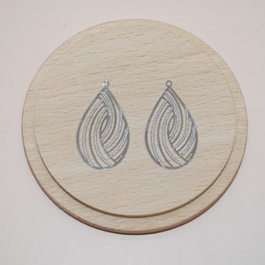 Può includere: Due basi per orecchini a forma di goccia d'acqua argentate con un design geometrico a spirale. Le basi sono su una superficie di legno.