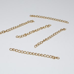May include: Five gold chain extenders, each with a different length, are laid out on a white surface.