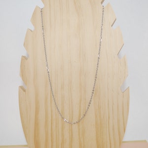 May include: A silver chain necklace on a wooden display stand.