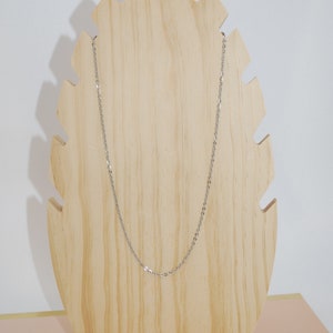 May include: A silver chain necklace displayed on a wooden stand. The chain is thin and delicate, with a simple design.