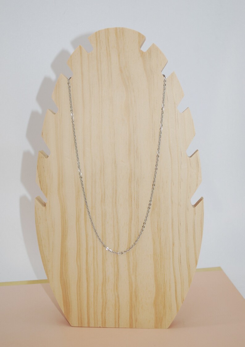May include: A silver chain necklace displayed on a wooden stand. The chain is thin and delicate, with a simple design.