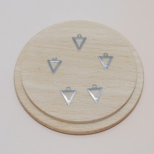 Peut inclure: Cinq breloques en forme de triangle argenté avec une boucle en haut, disposées sur une surface en bois.