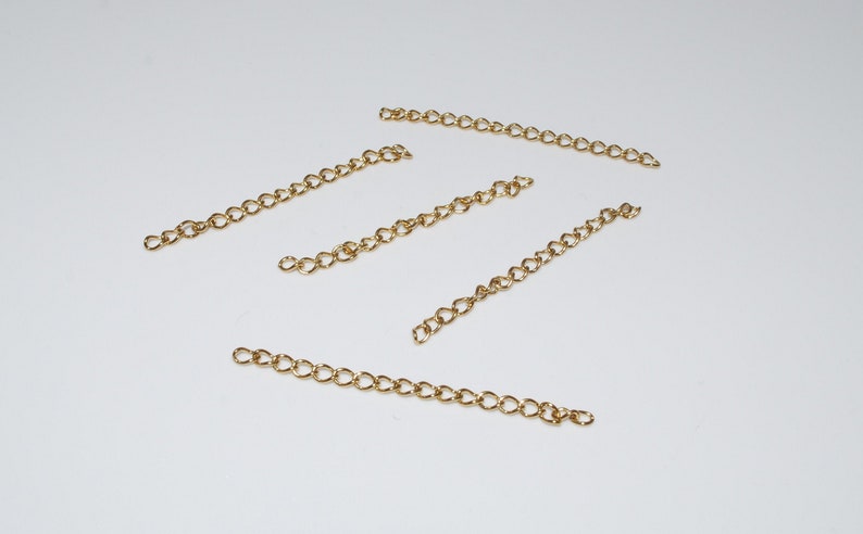 May include: Five gold chain extenders, each about 2 inches long, are laid out on a white surface.