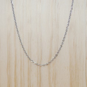 May include: A silver chain necklace on a wooden display stand.