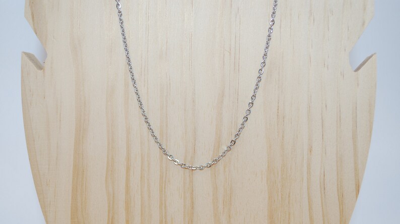 May include: A silver chain necklace on a wooden display stand.