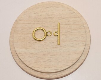 May include: A gold-colored toggle clasp set against a light wood grain background. The clasp consists of a circular ring and a straight bar with a small loop. The set is designed for jewelry making and crafting.