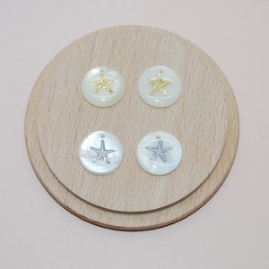 May include: Four white shell-shaped ornaments with a starfish design. Two ornaments have a gold starfish and two ornaments have a silver starfish.