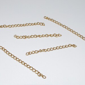 May include: Five gold chain extenders, each about 2 inches long, are laid out on a white surface.