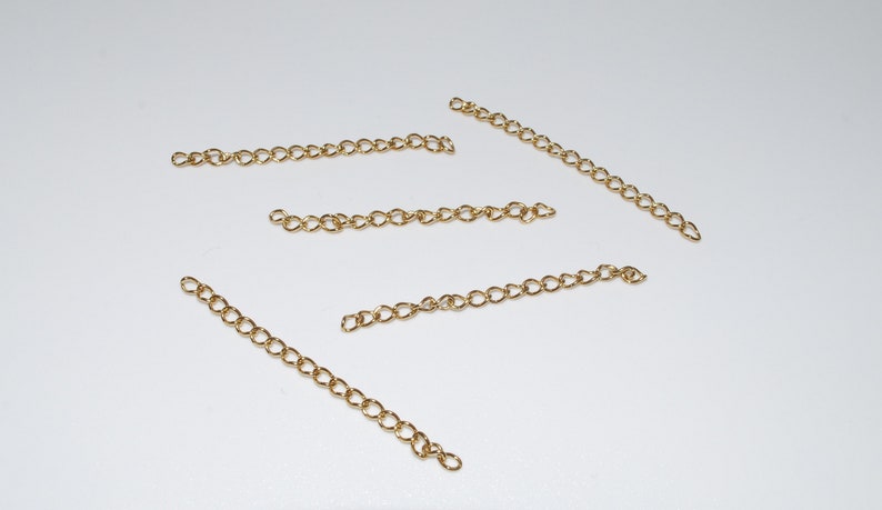 May include: Five gold chain extenders, each about 2 inches long, are laid out on a white surface.