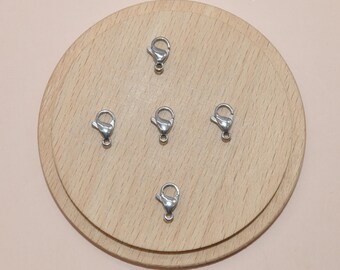 May include: Five silver-toned lobster clasps on a wooden surface. The clasps are used for jewelry making.