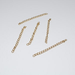 May include: Five gold chain extenders, each approximately 2 inches long, are laid out on a white surface.
