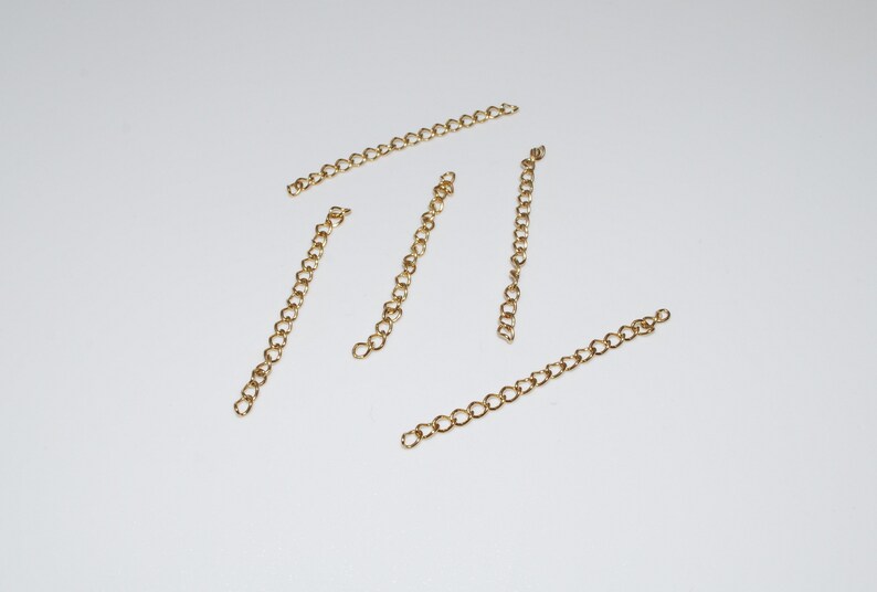 May include: Five gold chain extenders, each approximately 2 inches long, are laid out on a white surface.