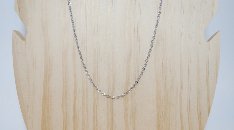 May include: A silver chain necklace on a wooden display stand.