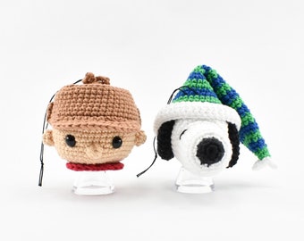 May include: Two crocheted ornaments, one of a boy wearing a brown hat and the other of a dog wearing a green and blue hat.