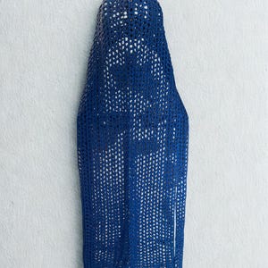 May include: A cobalt blue, open-weave crochet hood and shawl. The hood is rounded at the top and tapers down into a long, rectangular shawl. The crochet pattern creates a delicate, lacy effect. The shawl has two long, narrow extensions at the bottom.