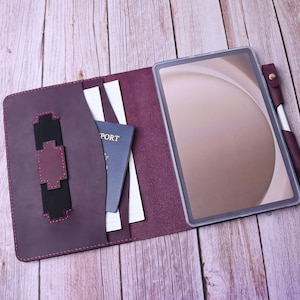 May include: A burgundy leather folio case with a built-in pen holder, a passport, and a tablet inside. The case has a flap that closes with a snap.