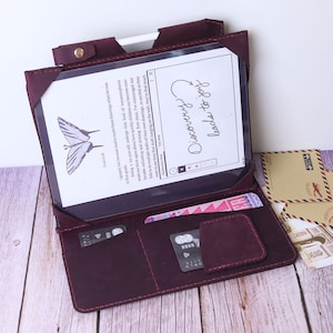 May include: Burgundy leather folio case with a tablet inside. The tablet screen shows a butterfly illustration and handwritten text that says "Discover the beauty of life". The case has a pocket for cards and a pen holder.