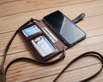 May include: A brown leather phone case with a strap. The case has slots for cards and cash. A smartphone is inside the case.