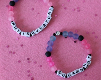 May include: Two beaded bracelets with pink, blue, and black beads. One bracelet spells "WHY IS EVERYONE" and the other spells "SO DAMN HOT".