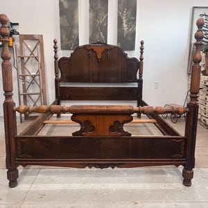 May include: A dark brown antique four-poster bed with ornate carvings on the headboard, footboard, and posts. The bed frame is made of wood and features a classic design, showcasing a vintage aesthetic. The bed is empty, ready for a mattress.