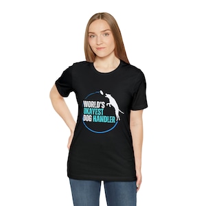 Może przedstawiać: Czarny t-shirt z biało-niebieską grafiką. Grafika przedstawia psa skaczącego po dysk, z napisem "WORLD'S OKAYEST DOG HANDLER" w niebieskim okręgu. Koszulka wykonana jest z miękkiego materiału.