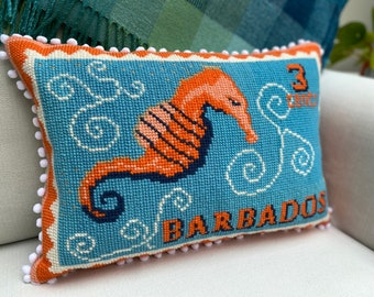Peut inclure: Un coussin en point d'aiguille bleu et orange avec une bordure blanche et des pompons. Le coussin représente un hippocampe et le texte "3 cents Barbados".