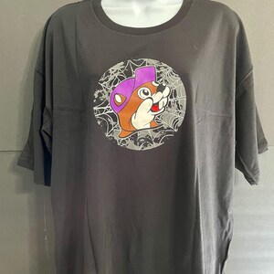 May include: Dark gray t-shirt featuring a cartoon beaver wearing a purple hat, set against a spiderweb design within a circle. The beaver has a friendly expression. The shirt is displayed on a white mannequin.