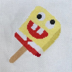 May include: A yellow popsicle with a smiling face and two large eyes. The popsicle is on a brown stick.