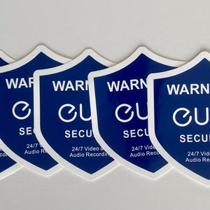 Puede incluir: Cinco pegatinas en forma de escudo azul y blanco con el texto "WARNING!! eufy SECURITY 24/7 Video and Audio Recording" en la pegatina más grande. Las pegatinas más pequeñas tienen el texto "WARNING! eufy SECURITY 24/7 Video and Audio Recording" y un logotipo "e" estilizado.