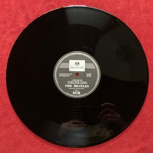 May include: A black vinyl record featuring a Parlophone label in the center. The text on the label reads Love Me Do, The Beatles, and includes details about the recording, production by George Martin, and the EMI record company logo.