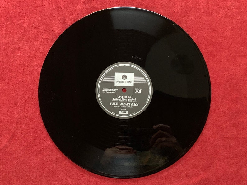 May include: A black vinyl record featuring a Parlophone label in the center. The text on the label reads Love Me Do, The Beatles, and includes details about the recording, production by George Martin, and the EMI record company logo.