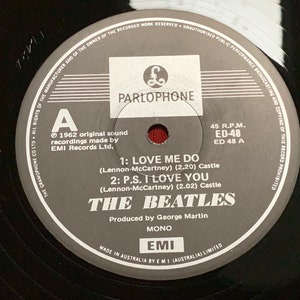 May include: A black vinyl record featuring the Parlophone label with the text "THE BEATLES". The record includes the songs "LOVE ME DO" and "P.S. I LOVE YOU". The label indicates it was produced by George Martin.