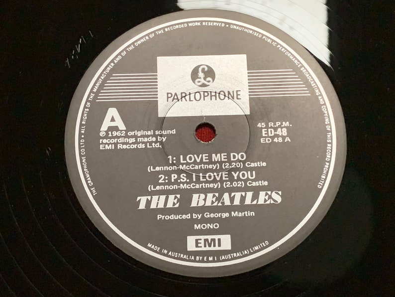 May include: A black vinyl record featuring the Parlophone label with the text "THE BEATLES". The record includes the songs "LOVE ME DO" and "P.S. I LOVE YOU". The label indicates it was produced by George Martin.