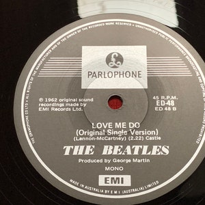 May include: A close-up of a black vinyl record featuring the Parlophone label. The label includes the text "LOVE ME DO" by The Beatles, produced by George Martin. The record is a 45 RPM single, made in Australia.