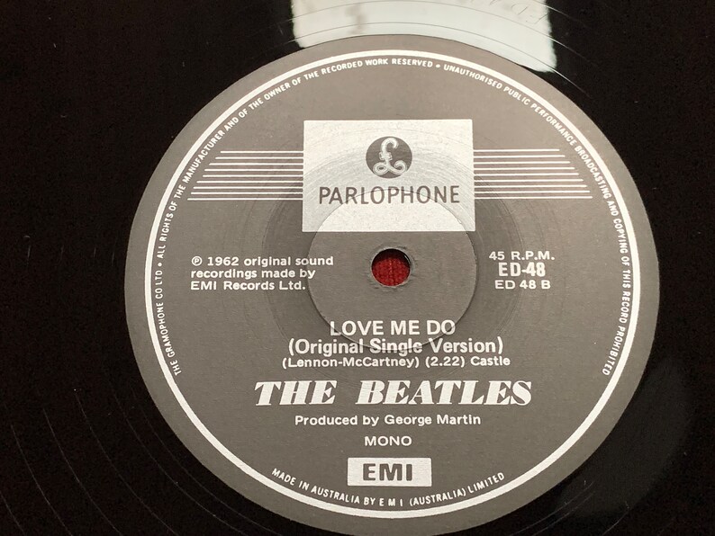 May include: A close-up of a black vinyl record featuring the Parlophone label. The label includes the text "LOVE ME DO" by The Beatles, produced by George Martin. The record is a 45 RPM single, made in Australia.