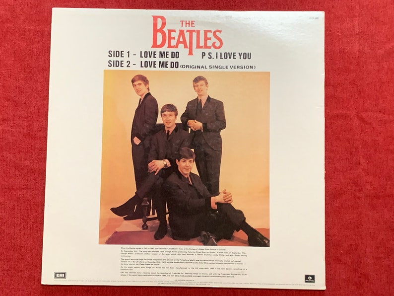 May include: Album cover for The Beatles' single, featuring the band members in black suits. The text reads "SIDE 1 - LOVE ME DO, SIDE 2 - LOVE ME DO, P.S. I LOVE YOU." The background is a light orange color.