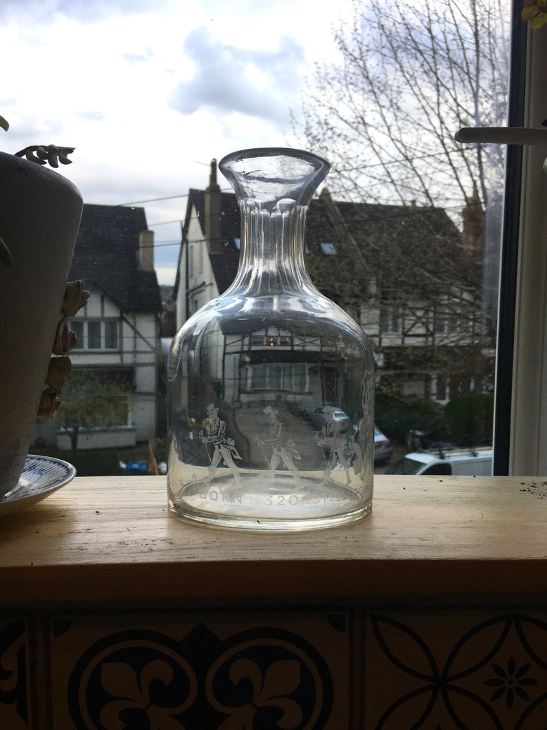 May include: A clear glass decanter with a textured surface and a wide mouth. The decanter has an etched design of three figures in formal attire. The text "JOHN 320" is etched on the bottom of the decanter.