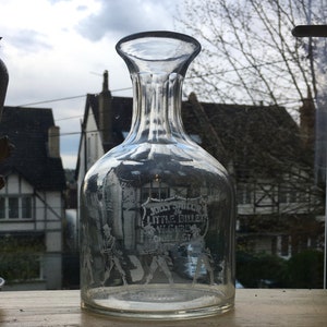 May include: A clear glass decanter with a textured surface and a label that reads "Jolly Sailor & Little Billet, Wycombe St."