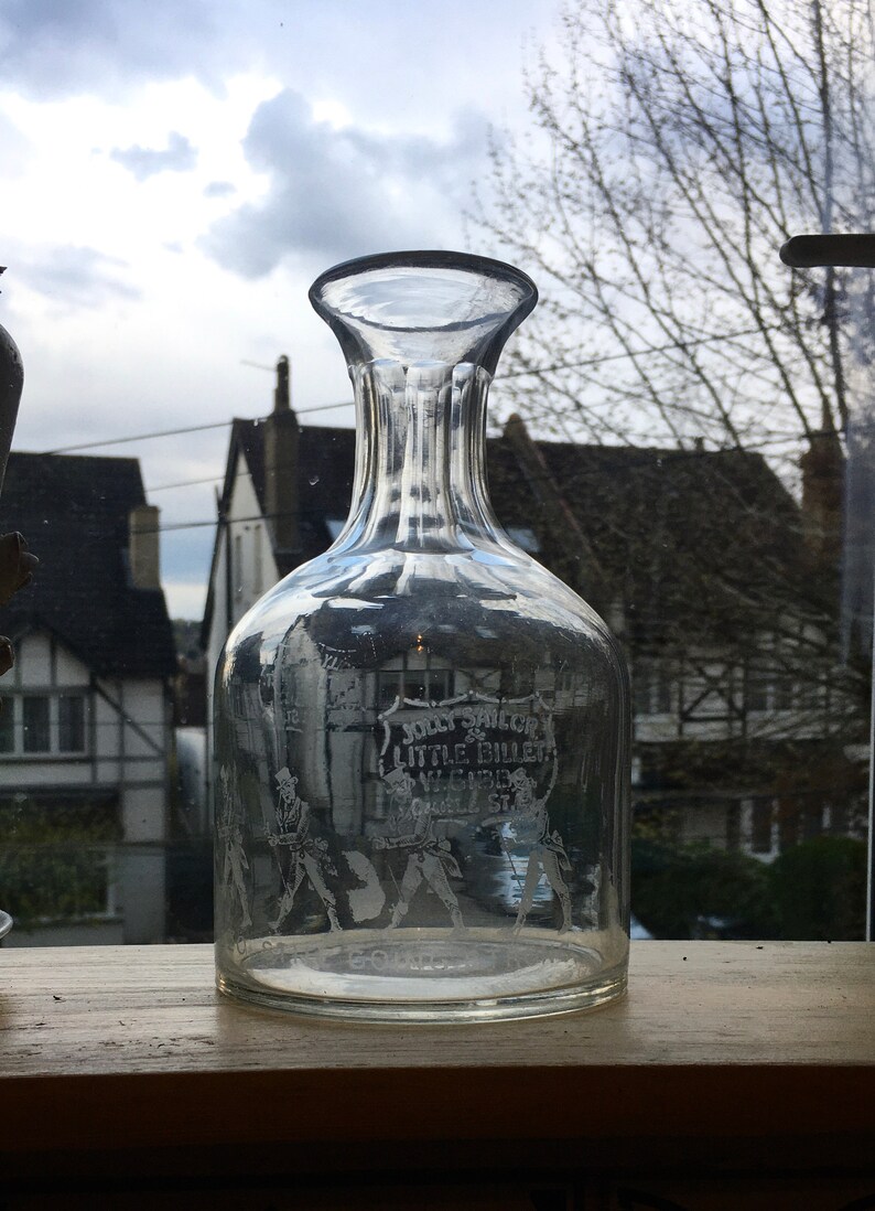 May include: A clear glass decanter with a textured surface and a label that reads "Jolly Sailor & Little Billet, Wycombe St."