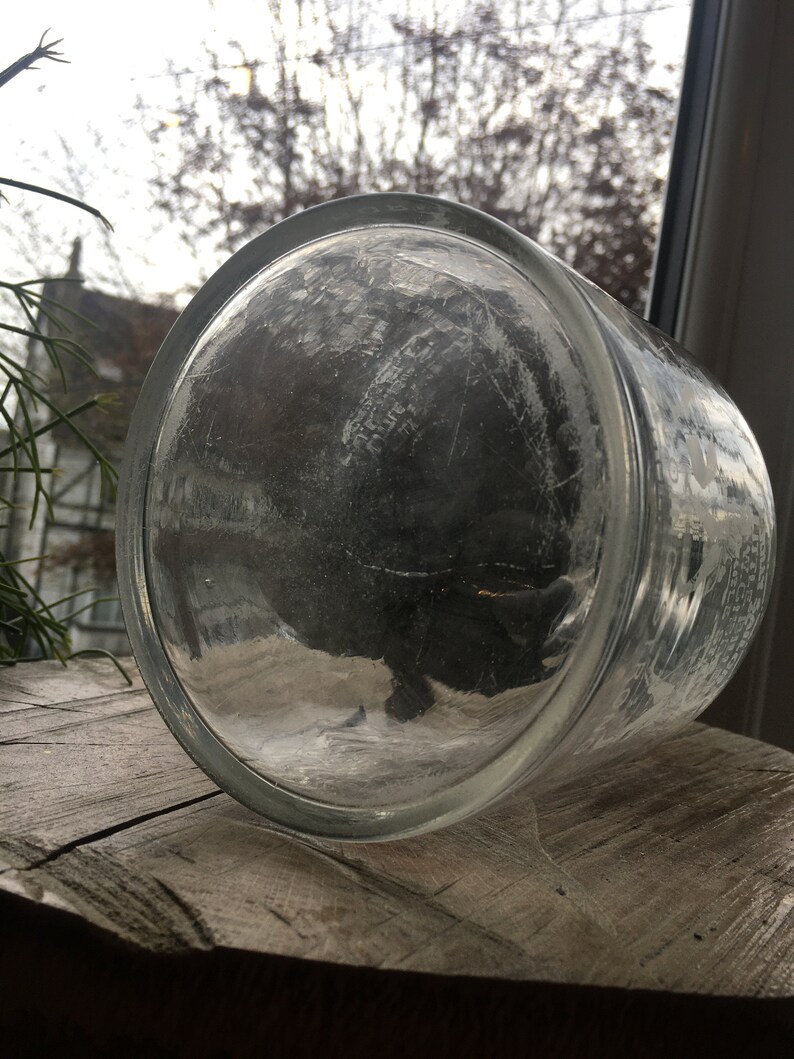 May include: A clear glass jar with a textured surface. The jar is empty and has a wide mouth.