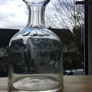 May include: A clear glass decanter with a textured neck and a wide base. The decanter has a label that reads "Jolly Sailor" and "Little Lever".