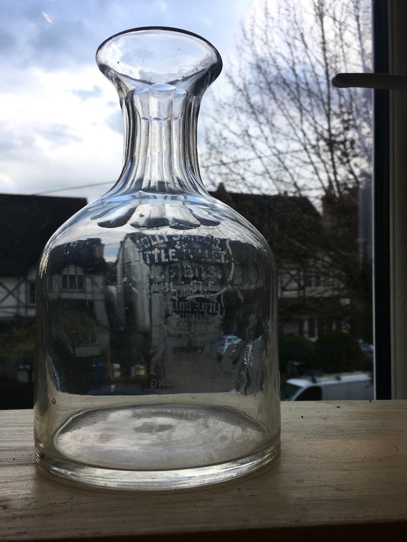 May include: A clear glass decanter with a textured neck and a wide base. The decanter has a label that reads "Jolly Sailor" and "Little Lever".