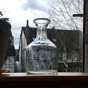 May include: A clear glass decanter with a textured surface and etched text that reads "Jolly Sailors Little Theatre" and "Still Going Strong".