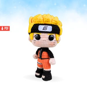 May include: A handmade crochet doll of a character with spiky yellow hair, a black headband, and an orange jumpsuit with black accents. The doll has large black eyes and small facial details. The background is a gradient of blue and white.
