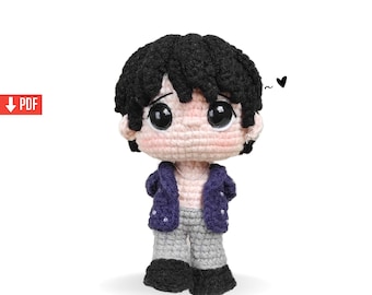 May include: A handmade crochet doll with black hair, large black eyes, and a light pink face. The doll wears a blue jacket, gray pants, and black shoes. A small black heart is drawn above the doll's head.