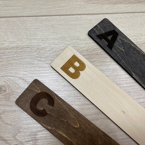 Puede incluir: Tres marcap&aacute;ginas de madera con las letras A, B y C grabadas. Los marcap&aacute;ginas son de diferentes tonos de marr&oacute;n.