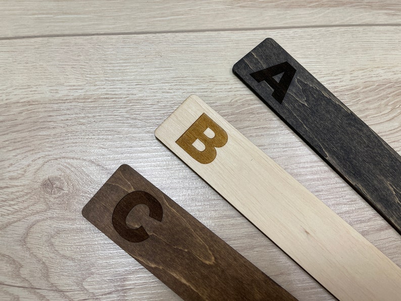 Puede incluir: Tres marcap&aacute;ginas de madera con las letras A, B y C grabadas. Los marcap&aacute;ginas son de diferentes tonos de marr&oacute;n.