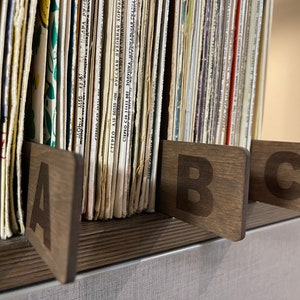 Puede incluir: Primer plano de un estante de madera con una colecci&oacute;n de discos de vinilo. Los discos est&aacute;n organizados por letra, con separadores de madera etiquetados con "A", "B" y "C".