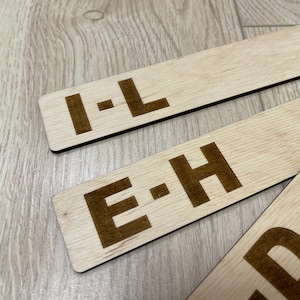 Puede incluir: Tres letreros de madera con letras negras. Los letreros dicen "I-L", "E-H" y "D".